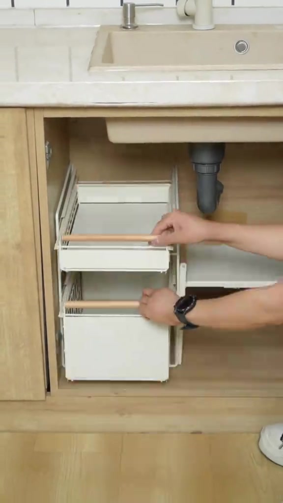Rak pull-out putih dua tingkat dipasang dalam kabinet bawah sinki, tangan menarik drawer