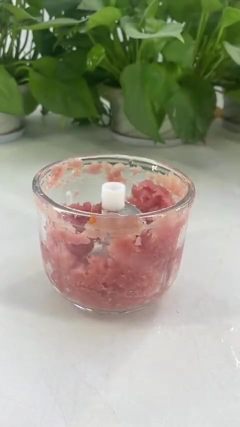 Mangkuk kaca chopper mini berisi daging cincang dengan mata pisau stainless steel di tengah