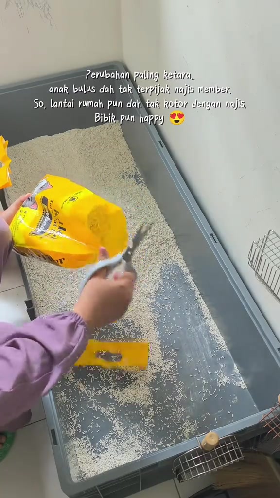 Tangan menggunting beg pasir kuning di atas bekas kelabu panjang berisi pasir, nampak saiz bekas berbanding badan orang