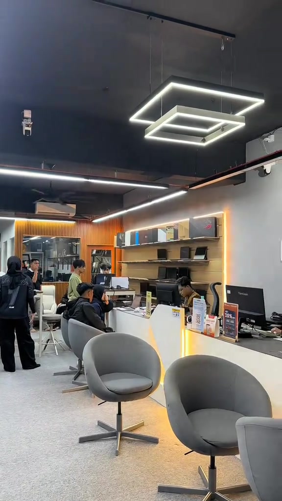 Ruang dalam kedai komputer Mechanize dengan kaunter servis, rak laptop di dinding dan beberapa pelanggan duduk menunggu