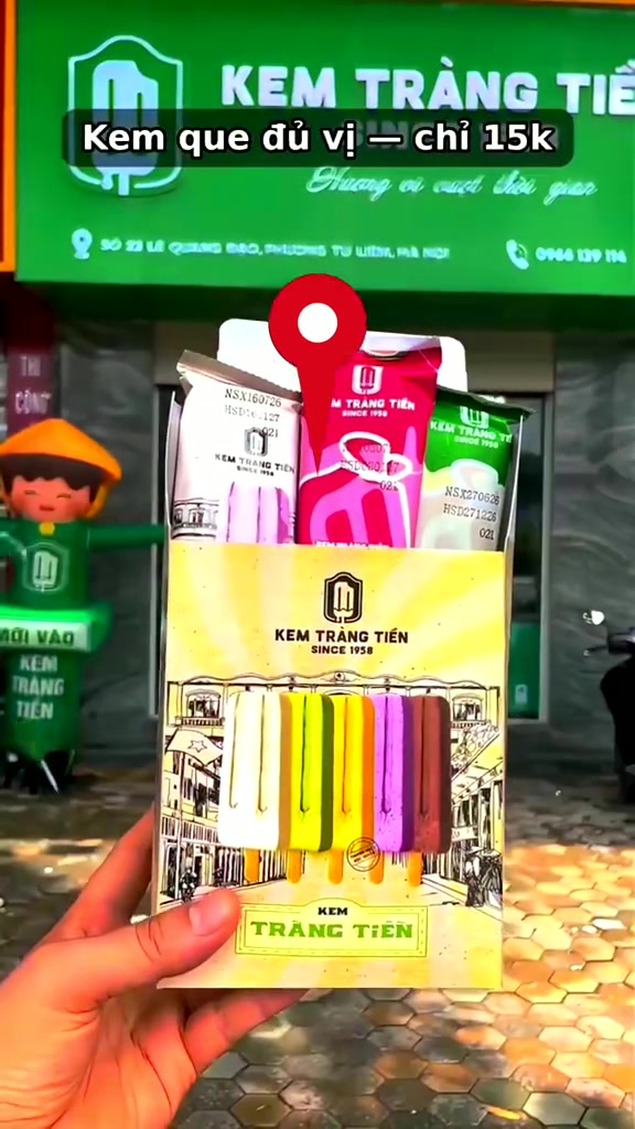 Hộp kem que Kem Tràng Tiền đủ màu cầm trước biển hiệu xanh của tiệm tại số 23 Lê Quang Đạo, Hà Nội