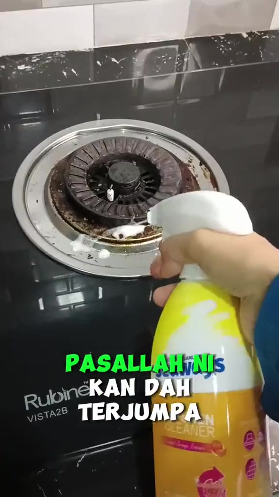 Tangan menyembur pencuci dapur berbusa ke arah burner dapur gas yang berkerak minyak