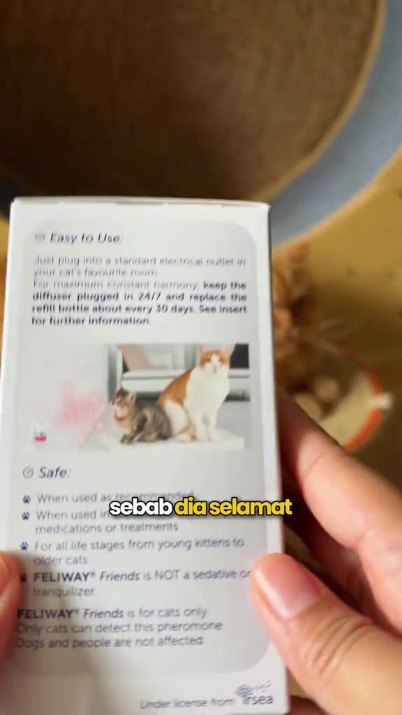 Tangan memegang kotak Feliway Friends yang menunjukkan arahan pakai: pasang pada soket, kekalkan terpasang 24/7, tukar refill setiap 30 hari, dan ia bukan ubat penenang