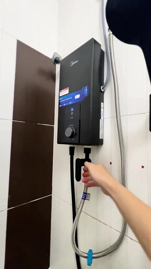 Tangan membuka injap air di bawah unit water heater Midea sebelum hidupkan kuasa