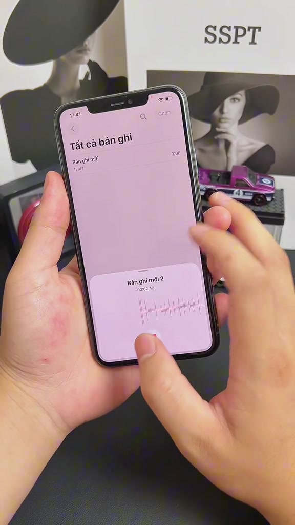 Một tay cầm chiếc iPhone mở ứng dụng ghi âm với danh sách bản ghi