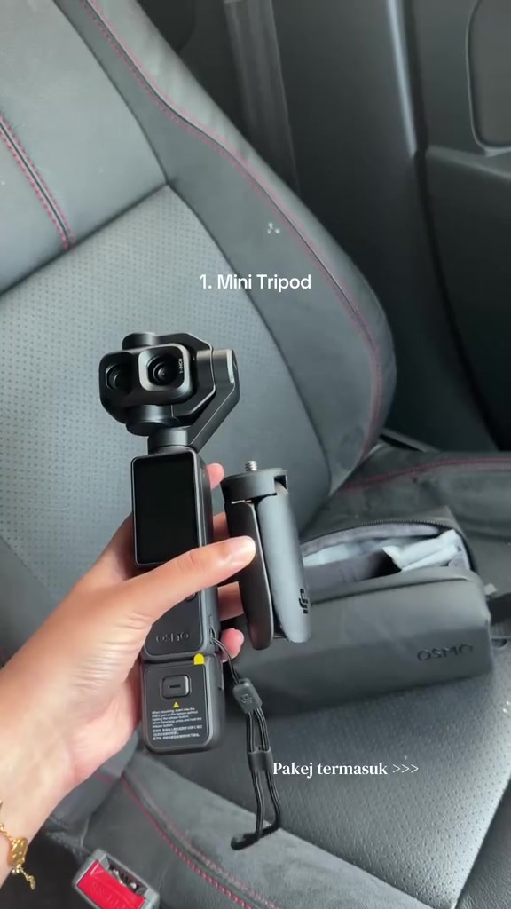 Tangan memegang Osmo Pocket 4P warna hitam bersama mini tripod dan beg galas Osmo di atas tempat duduk kereta
