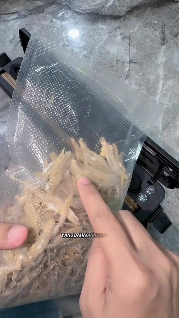 Beg vacuum bertekstur embossed berisi ikan bilis kering di atas mesin, jari menunjuk permukaan beg
