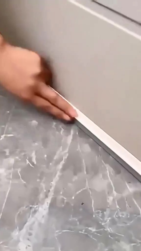 Tangan menekan jalur seal putih di celah bawah pintu pada lantai jubin marmar