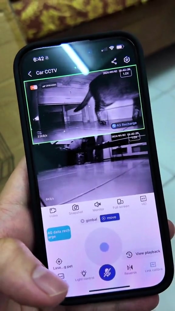 Skrin telefon menunjukkan aplikasi CCTV dengan rakaman kucing dalam mod penglihatan malam di ruang tamu, bersama butang rakaman, suara dan kawalan pan/tilt