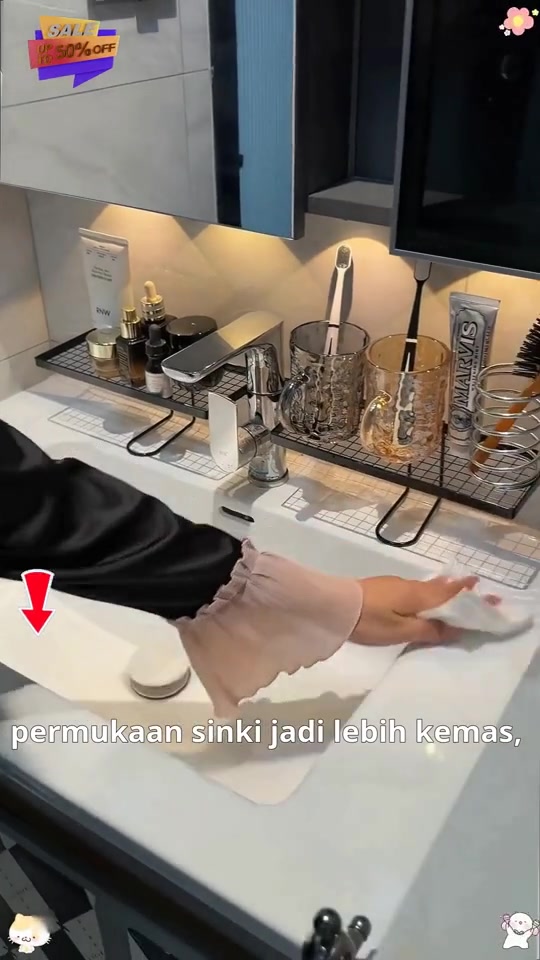 Rak grid hitam di tepi sinki memegang botol dan cawan, tangan sedang lap permukaan sinki