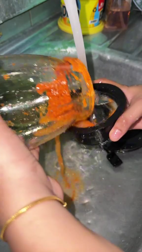 Tangan membilas jar blender bersisa pes cili di bawah paip sinki, bahagian bawah jar dibuka untuk cuci