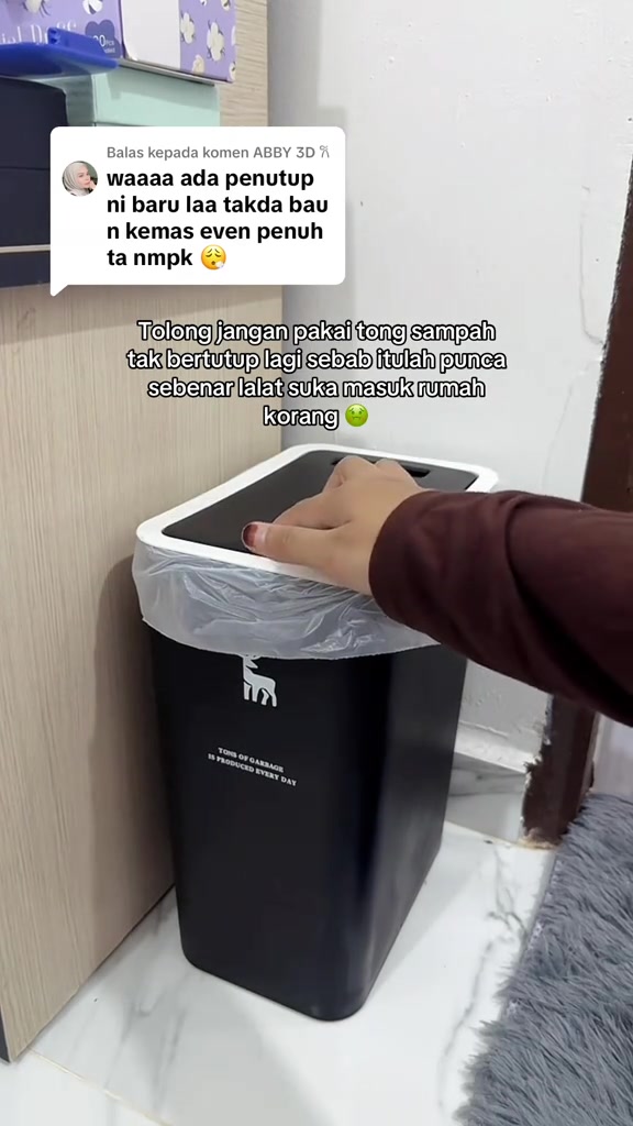 Tangan menekan penutup tong sampah slim hitam bertutup putih yang diletakkan rapat di sisi kabinet