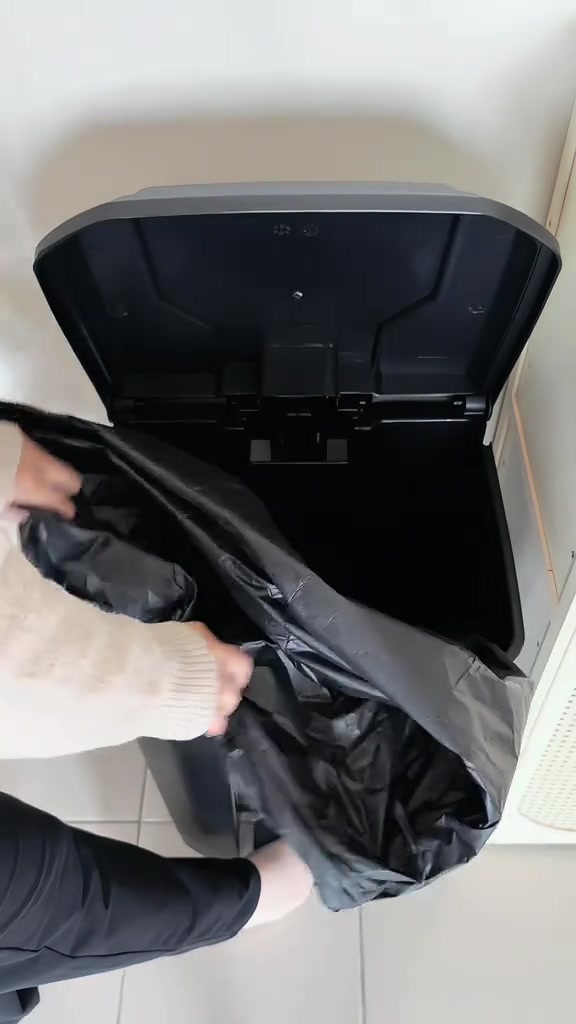 Dua tangan memasang beg plastik hitam ke dalam tong sampah pedal, pandangan dari atas nampak mekanisme penutup terbuka