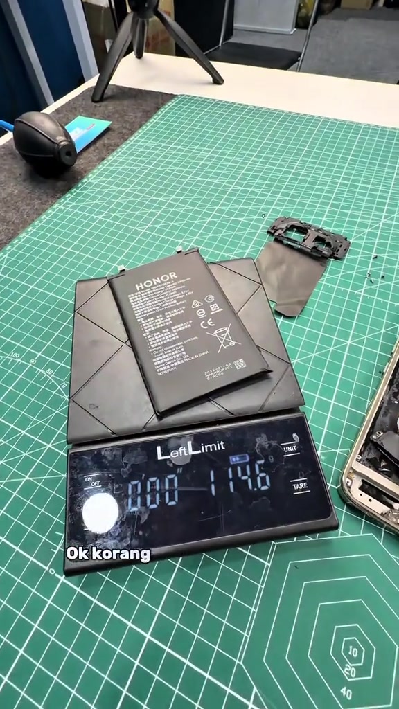 Bateri HONOR daripada phone diletak atas penimbang digital yang menunjukkan bacaan kira-kira 114 gram