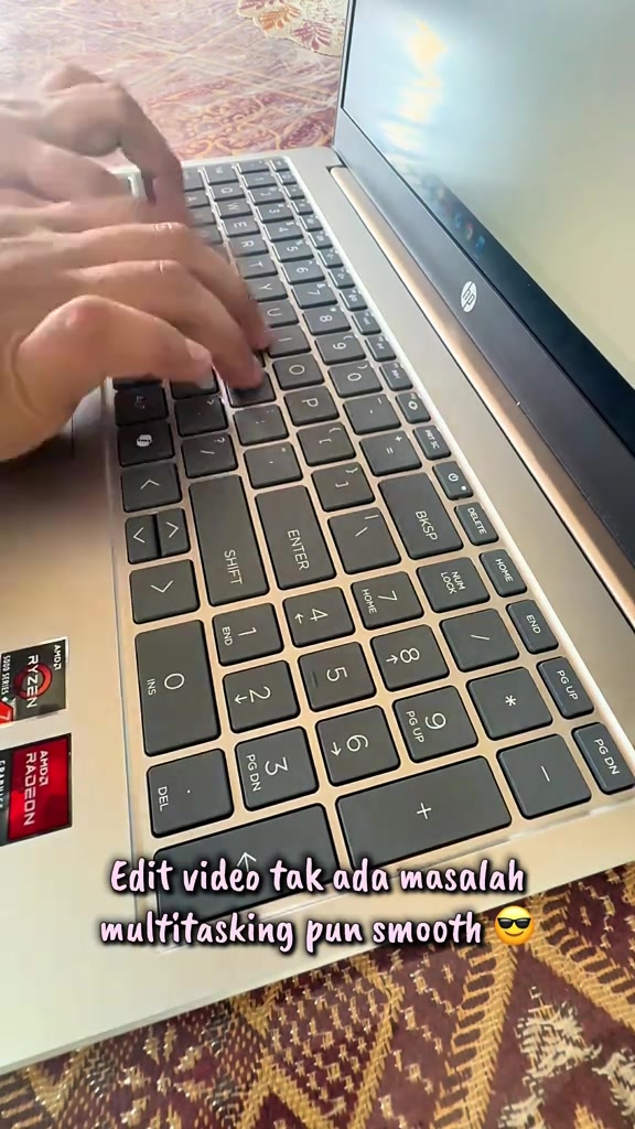 Tutup dekat jari menaip pada keyboard HP 15 dengan numpad, pelekat AMD Ryzen dan Radeon kelihatan di palm rest