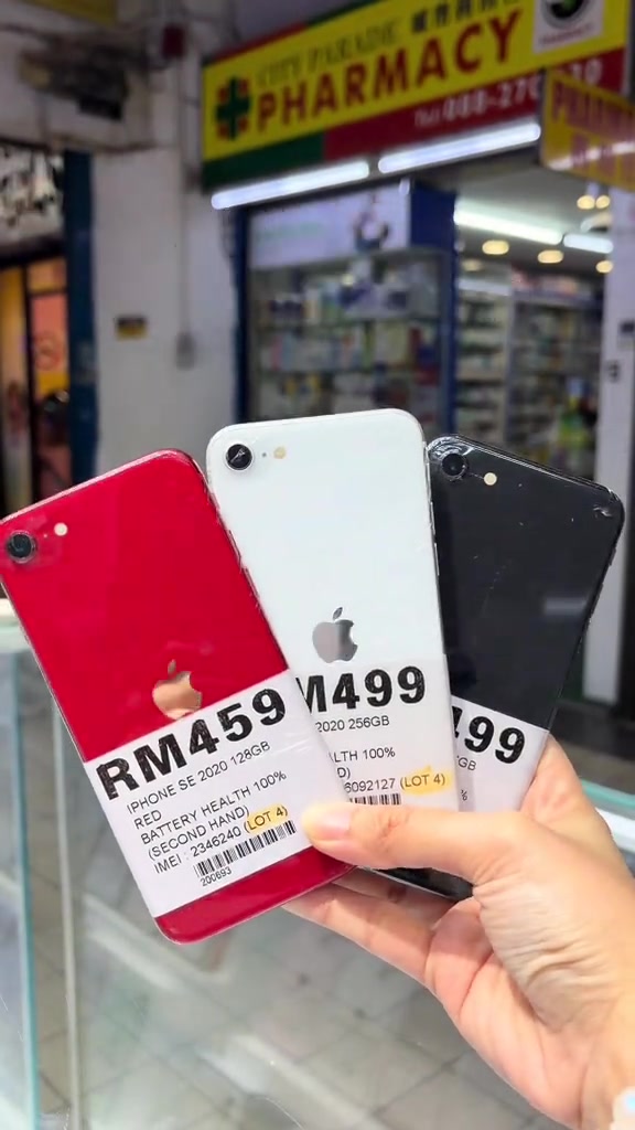 Tiga iPhone SE 2020 secondhand warna merah, putih dan hitam dipegang sebelah tangan dengan sticker RM459 dan RM499