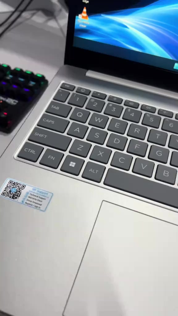Tutup dekat keyboard dan trackpad laptop HP 15 warna perak dengan pelekat sokongan HP di palm rest