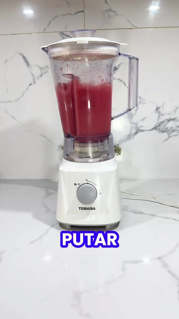 Blender Toshiba berwarna putih sedang mengisar jus merah dalam jar, tombol kelajuan pada badan mesin