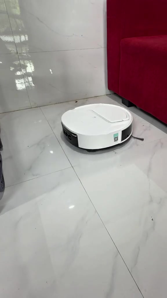 Robot hút bụi màu trắng đứng giữa sàn gạch bóng cạnh ghế sofa đỏ
