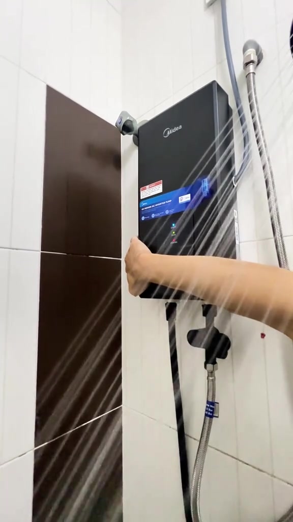 Water heater Midea di dinding dengan semburan air kuat dari kepala shower dan tangan di panel