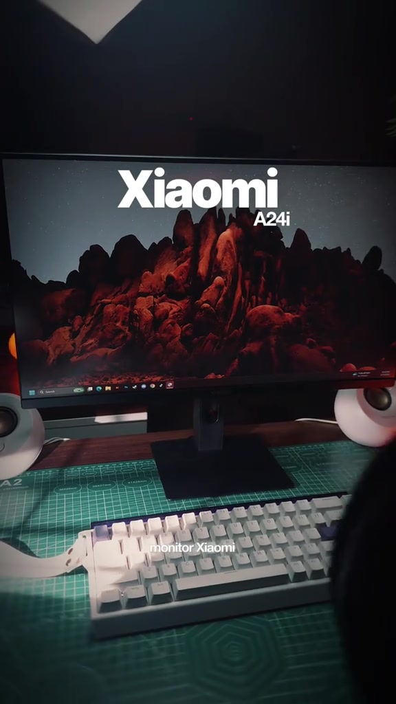 Monitor Xiaomi A24i di atas meja kerja dengan papan kekunci putih dan wallpaper gunung pada skrin