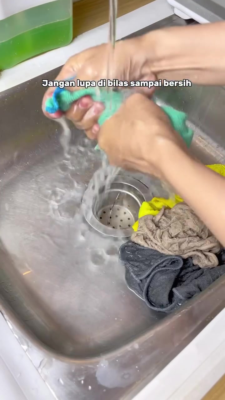 Tangan membilas kain dapur di bawah air mengalir dalam sinki stainless