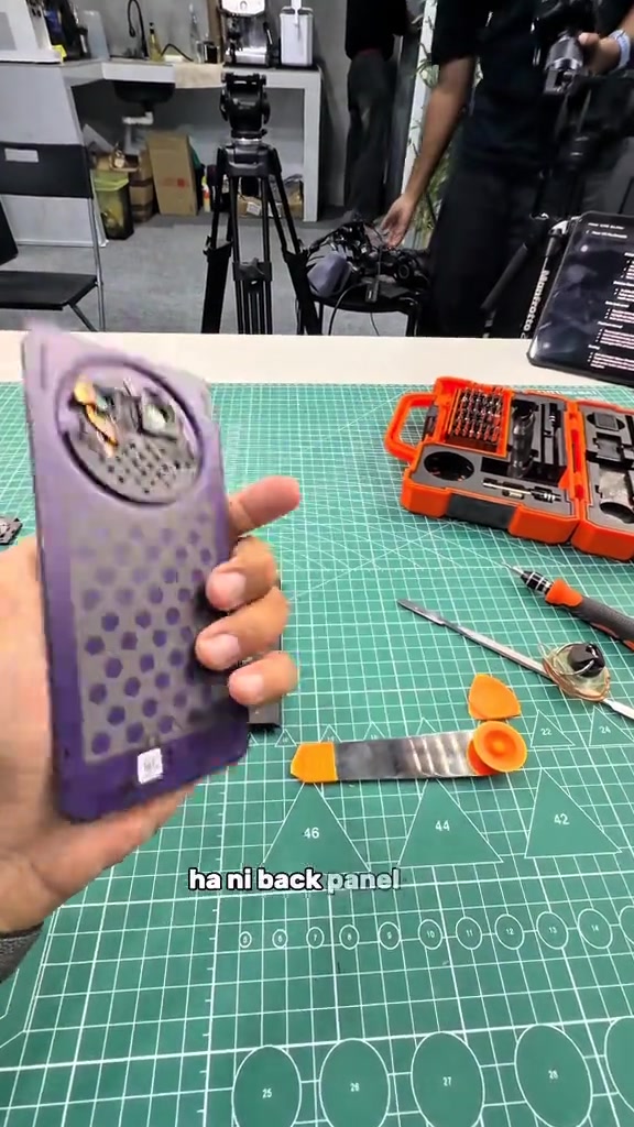 Back panel HONOR X9e Pro yang telah dibuka dipegang di atas tikar kerja hijau dengan set pemutar skru di sebelah