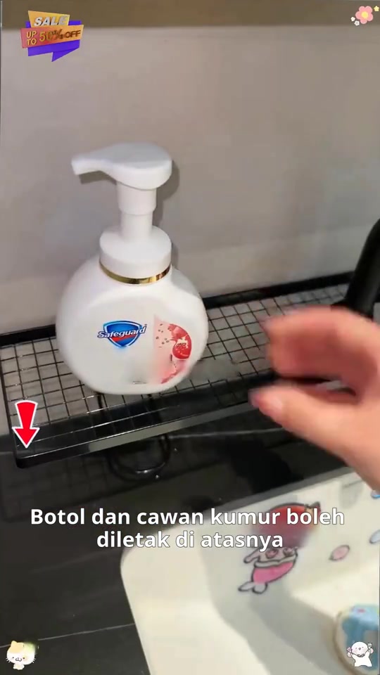 Botol sabun pam di atas rak grid hitam di tepi sinki, tangan sedang menyentuh rak