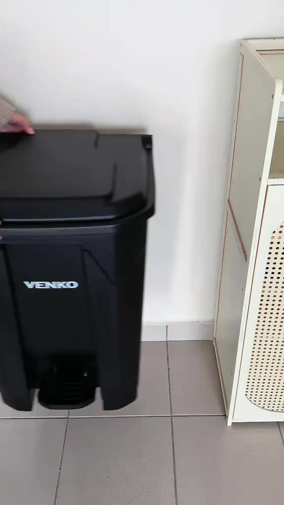 Tangan menutup penutup tong sampah pedal plastik hitam di sisi kabinet putih