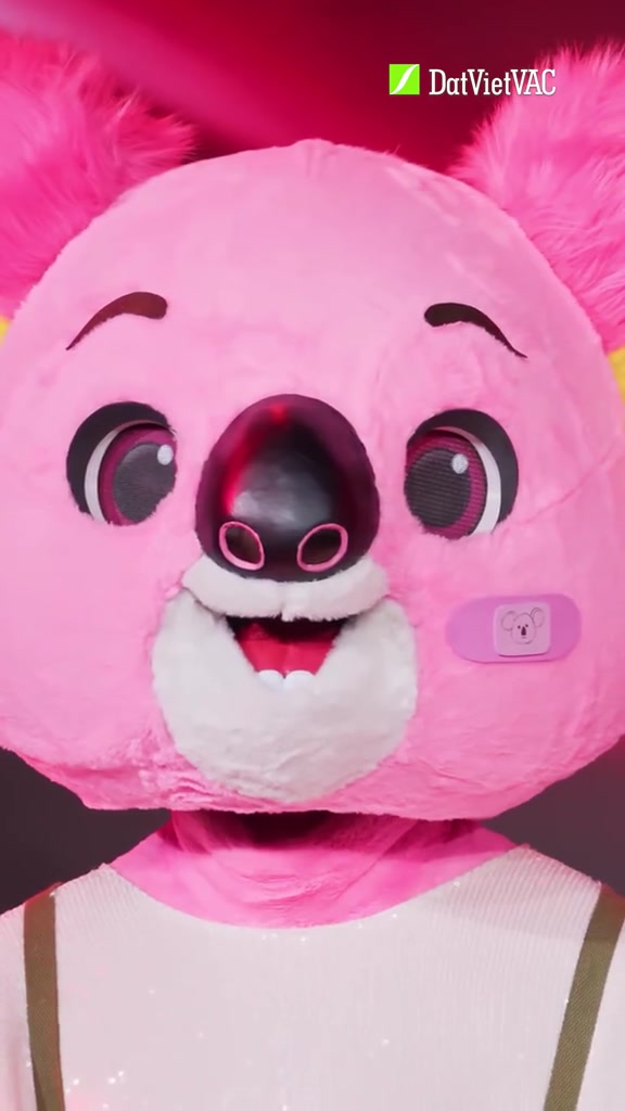 Cận cảnh mascot Koalaoke đầu gấu hồng tươi, mũi đen và má hồng trên nền đèn hồng