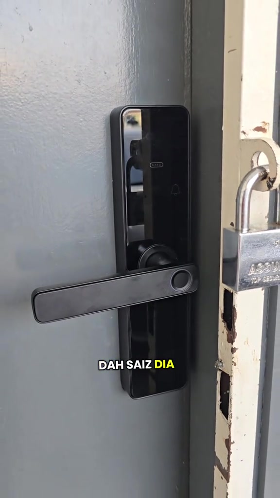 Smart lock hitam dengan keypad dan pemegang dipasang pada pintu logam kelabu, mangga besi tergantung pada rangka pintu di sebelah