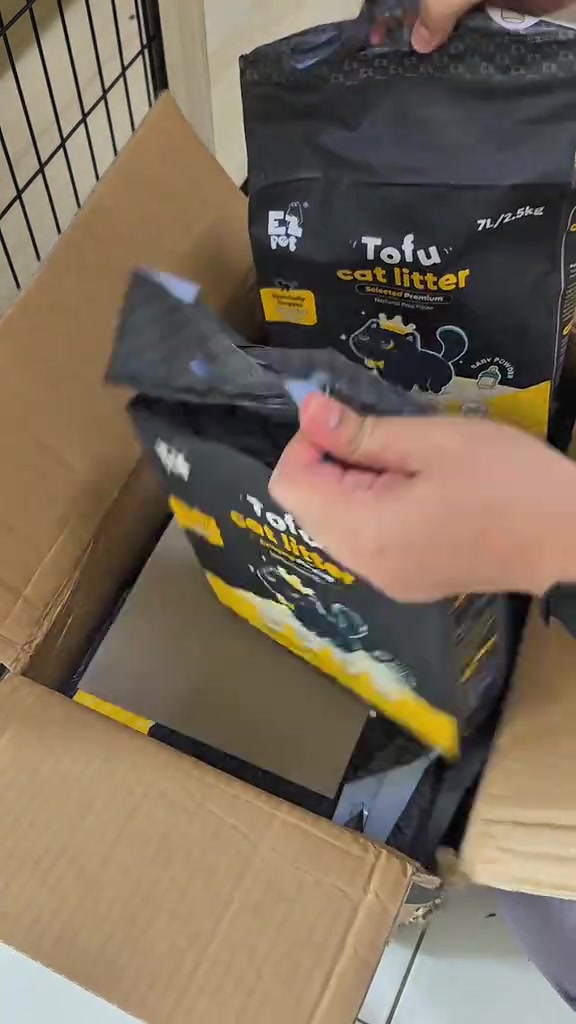 Tangan membuka beg hitam pasir kucing tofu berlabel 7L/2.5kg di atas kotak kadbod