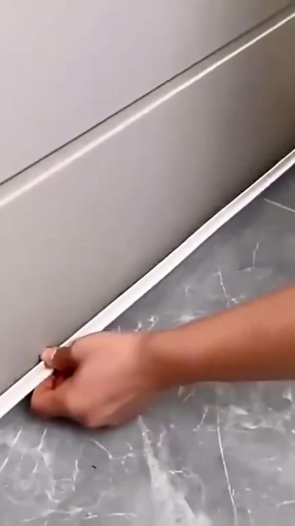 Tangan melekatkan jalur seal self-adhesive putih sepanjang bahagian bawah pintu pada lantai marmar kelabu