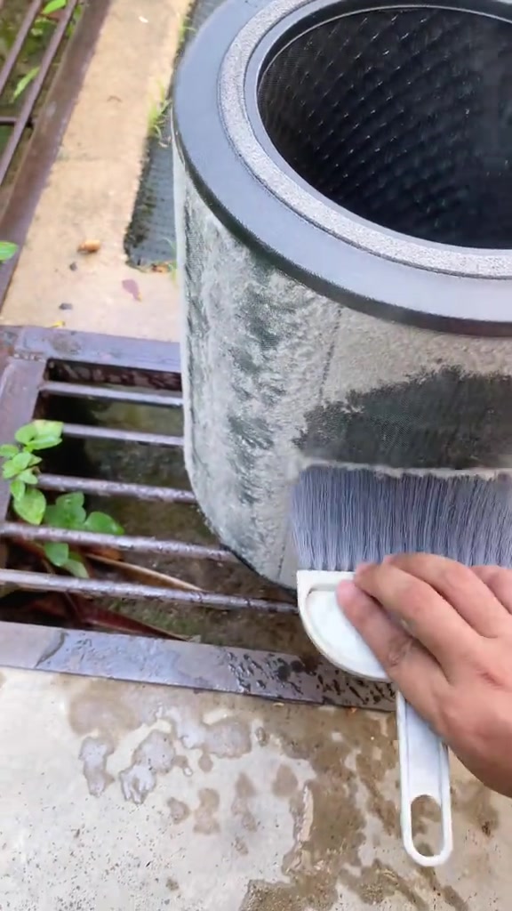 Penapis silinder penuh habuk kelabu sedang dibersihkan dengan berus kecil di luar rumah
