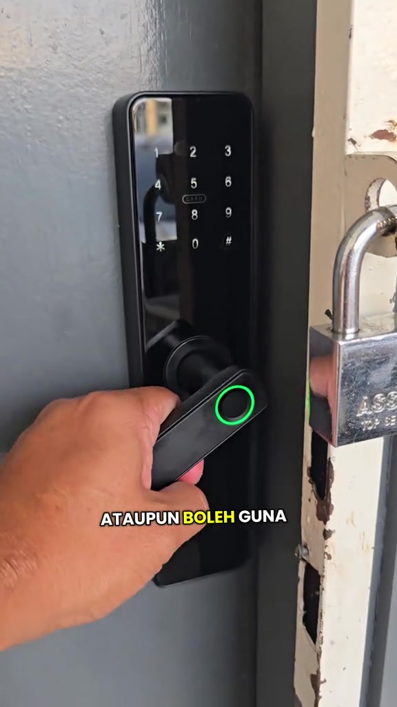 Tangan menekan pemegang smart lock dengan cincin cap jari bercahaya hijau, keypad nombor pada badan kunci hitam di pintu kelabu