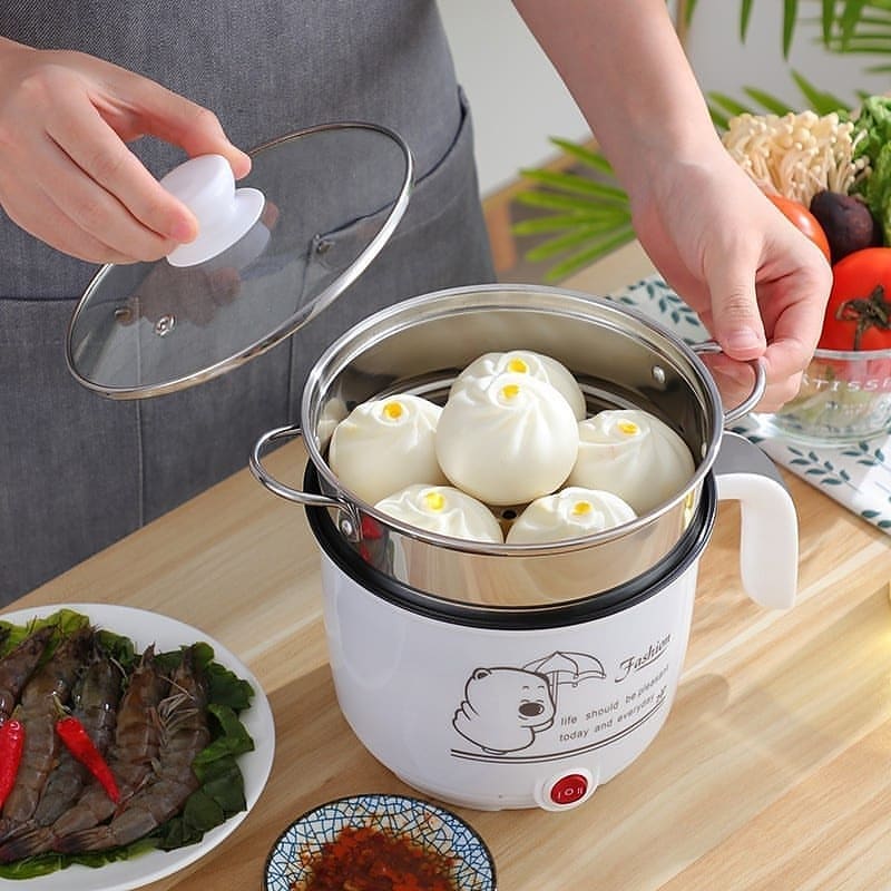 Mini multicooker putih dengan tray steamer stainless steel berisi pau, penutup kaca sedang diangkat tangan