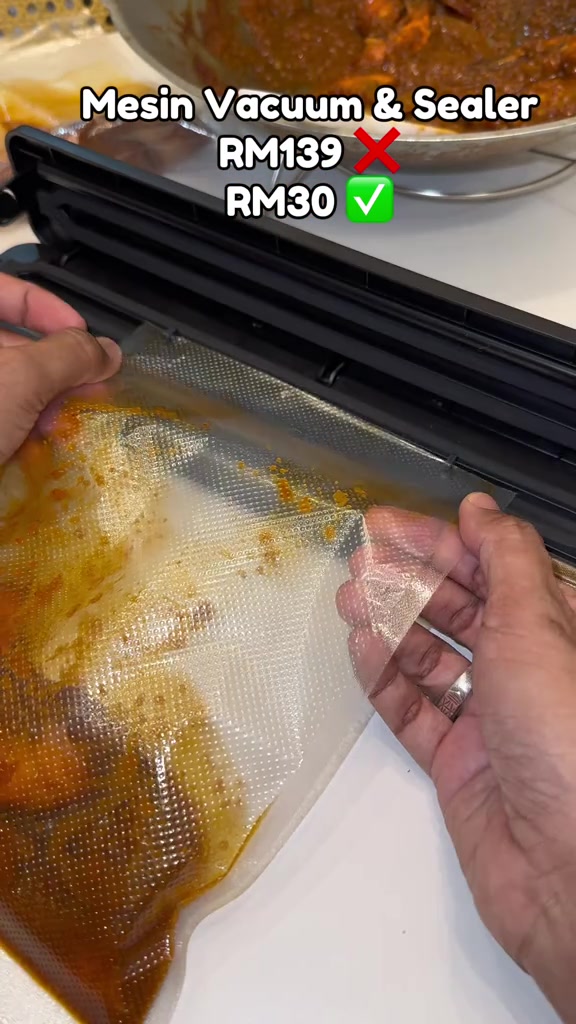 Dua tangan memasukkan beg vacuum berisi lauk berkuah ke dalam mesin vacuum sealer yang terbuka
