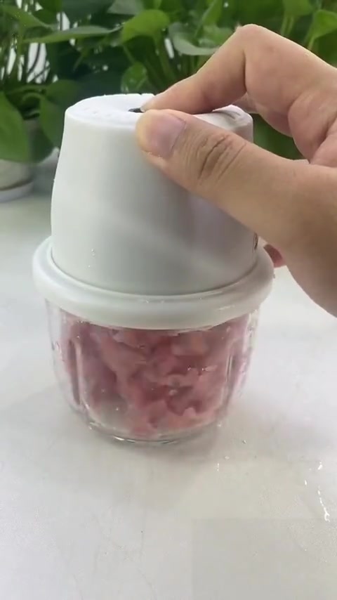 Tangan menekan penutup chopper mini putih berisi daging cincang dalam mangkuk kaca