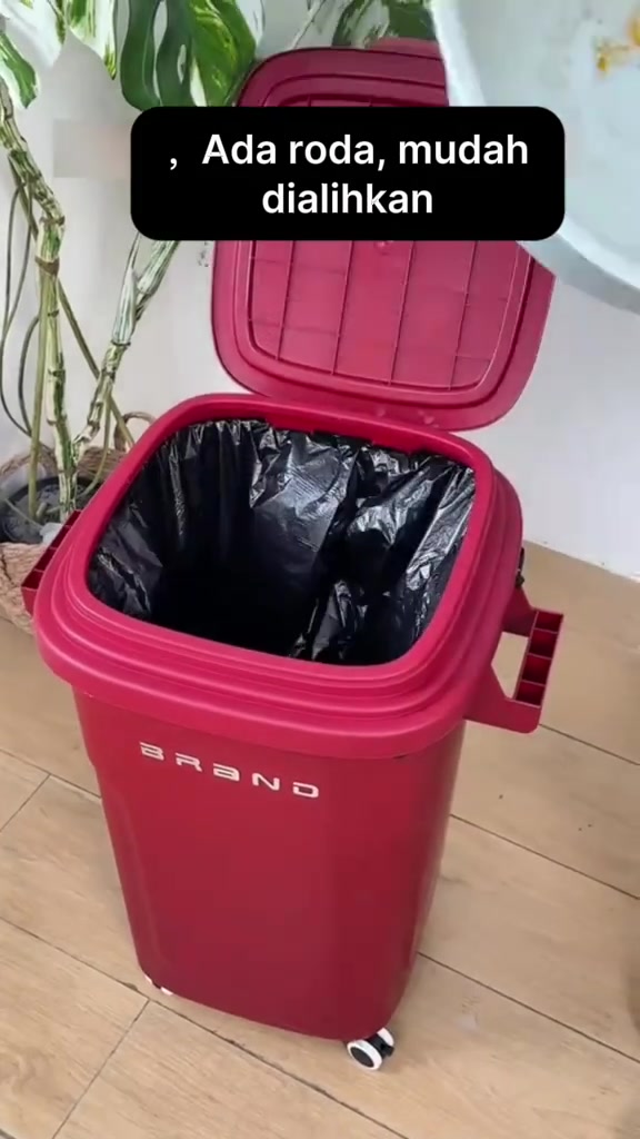 Tong sampah merah bertutup hinge dengan roda dan pemegang sisi, penutup terbuka nampak beg plastik hitam di dalam