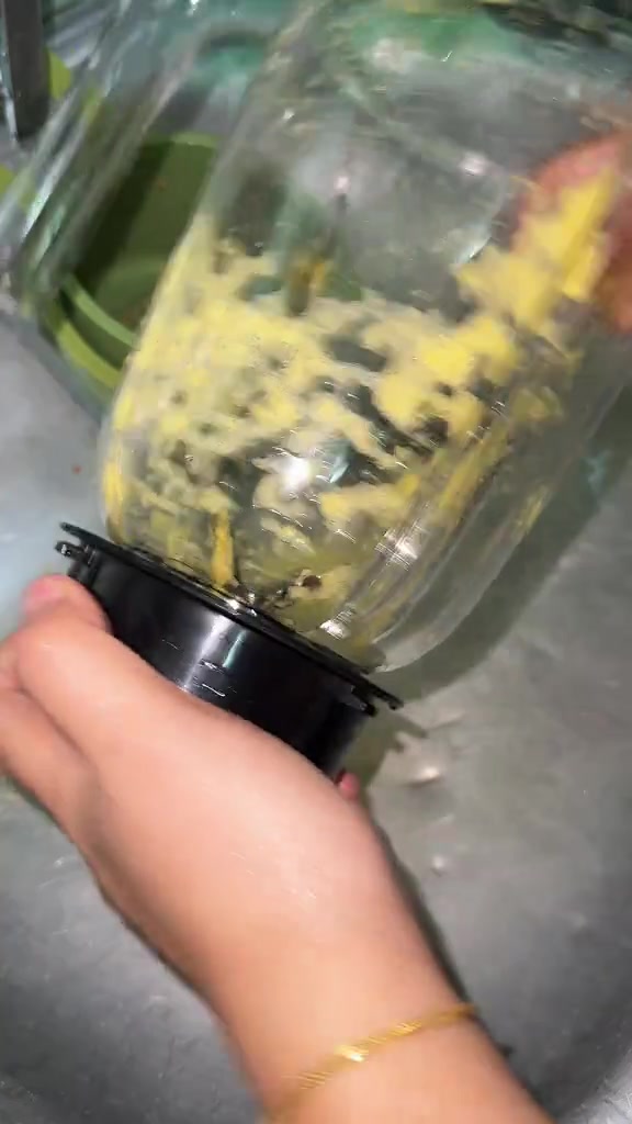 Tangan memegang bahagian bawah jar blender dengan pes kuning melekat pada dinding jar selepas dikisar