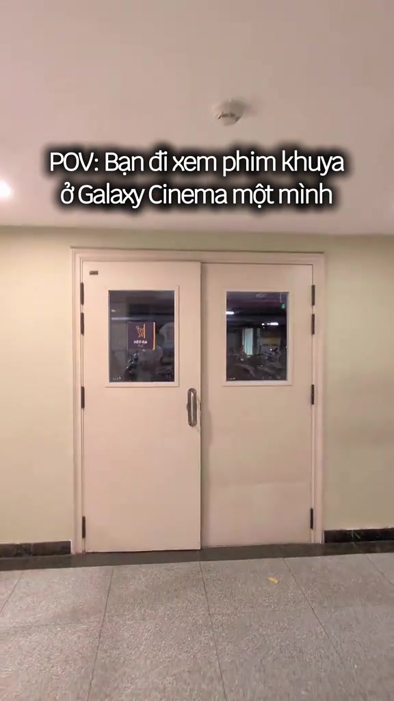 Cửa đôi màu kem dẫn vào phòng chiếu rạp Galaxy lúc vắng người, qua ô kính thấy hàng ghế trong phòng
