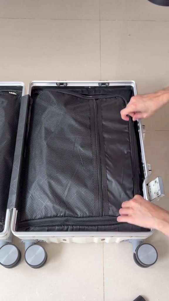 Sepasang tangan menutup zip pemisah mesh di dalam koper keras berwarna putih yang terbuka