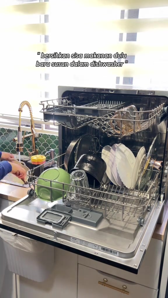 Rak mesin basuh pinggan tabletop penuh dengan pinggan, mangkuk, periuk kecil dan gelas, rak atas ditarik keluar di dapur berkonter kayu