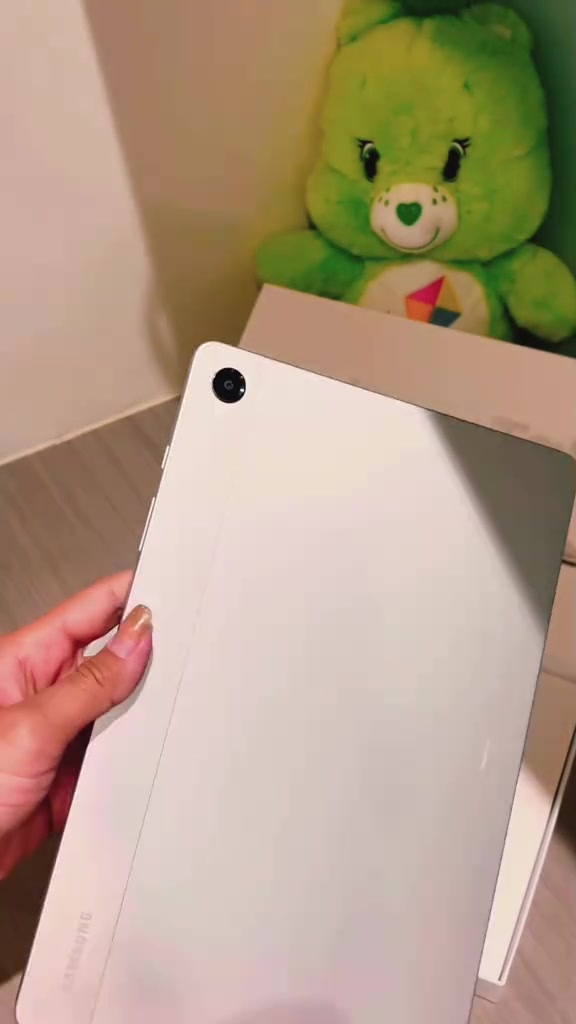 Mặt lưng màu bạc của máy tính bảng Samsung Galaxy Tab với một camera ở góc trên, đang được cầm trên tay trước hộp máy