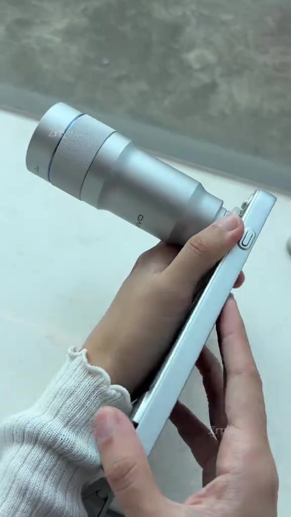 Tangan memegang ZEISS Telephoto Extender perak yang dipasang pada sisi vivo X500 Pro Max
