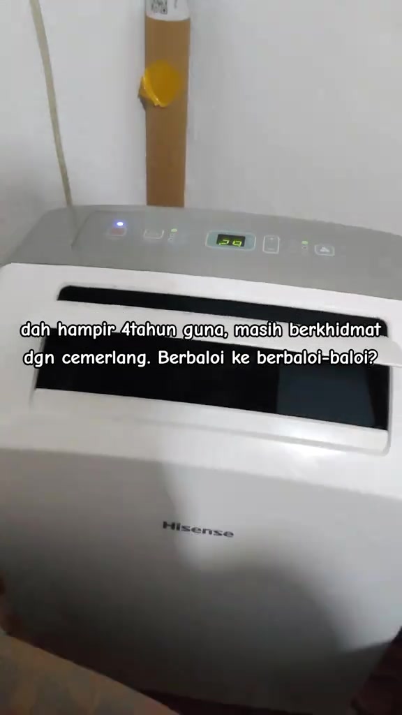 Bahagian atas portable aircond Hisense dalam bilik dengan paparan suhu dan hose dibalut cardboard di belakang