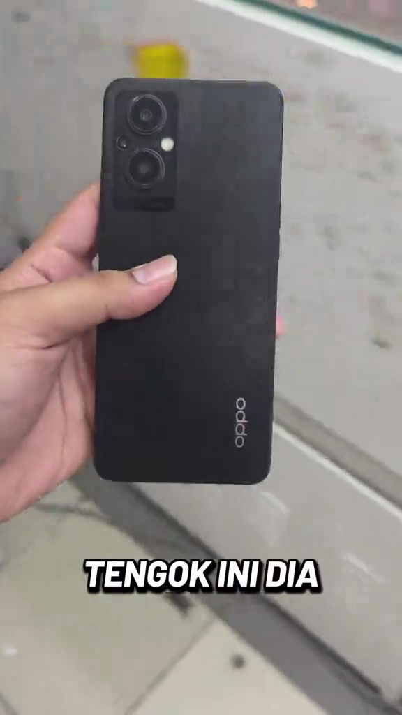 Belakang phone hitam OPPO Reno7 Z 5G dipegang di dalam kedai, modul dua kamera dan logo OPPO kelihatan jelas