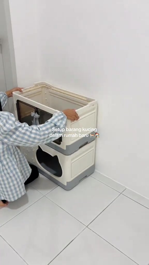 Sepasang tangan menyusun rumah kucing plastik bertingkat di sudut dinding unit rumah baru yang masih kosong