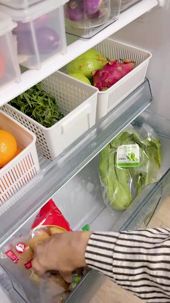 Bahagian dalam peti sejuk dengan bakul putih berlubang berisi kangkung, jambu batu dan buah naga, serta laci sayur berisi pak choi berbalut plastik