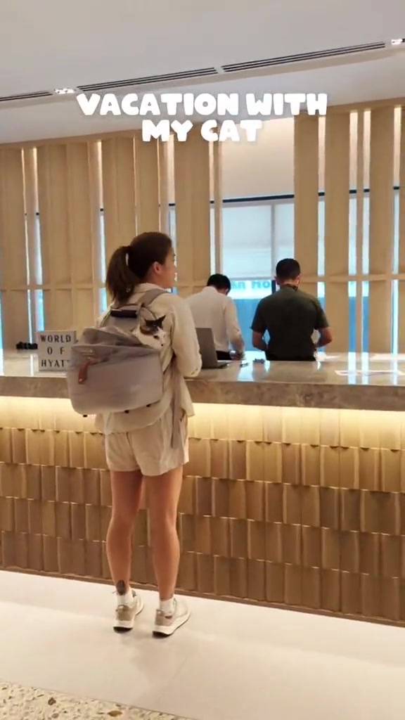 Seorang tetamu berdiri di kaunter penerimaan hotel dengan kucing dalam beg galas carrier di belakangnya